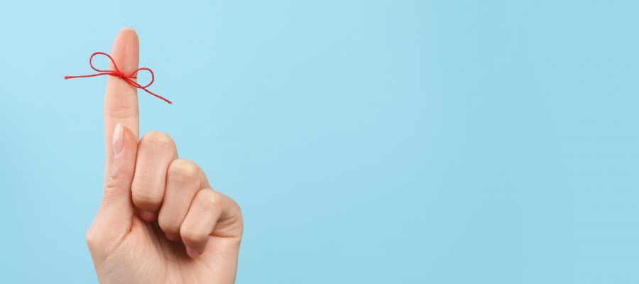 Finger with red string tied around it in front of blue background